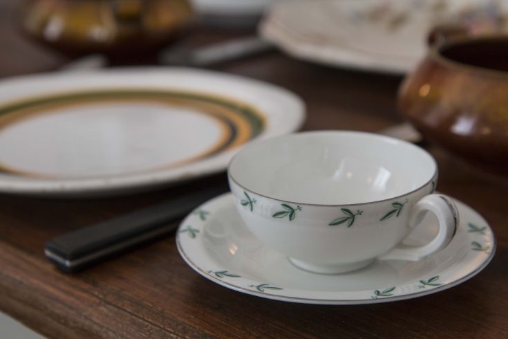 A decorated porcelain cup rests on a wooden table, surrounded by plates in a cozy atmosphere.