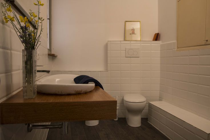 Spacious and well-lit bathroom with wooden and ceramic elements, featuring a flower vase.
