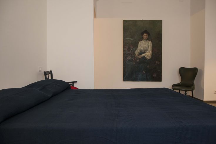 A spacious B&B room with a double bed, a green chair, and a picture hanging on the wall.