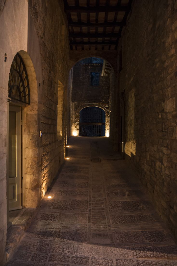 A charming alley in a historical center, bathed in warm light, with stone walls.