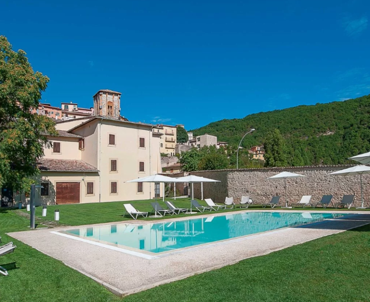 Piscina e giardino di un hotel circondato dalla natura, con panorama sulle colline circostanti.