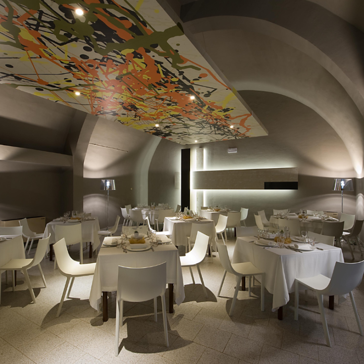 Interno di un ristorante semplice con tavoli apparecchiati e un soffitto decorato.