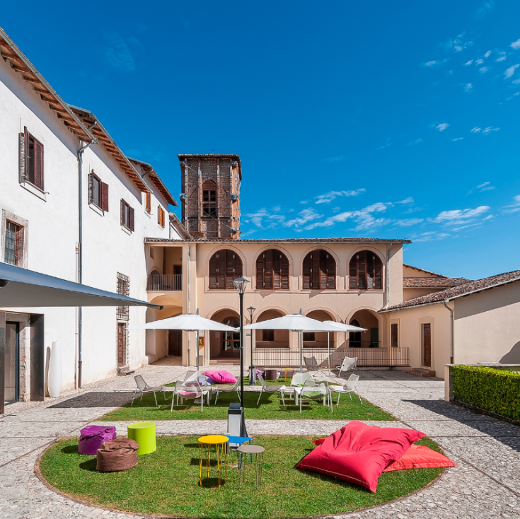Un'area esterna con arredi vivaci, circondata da piante e con una scena che mostra il campanile sullo sfondo.