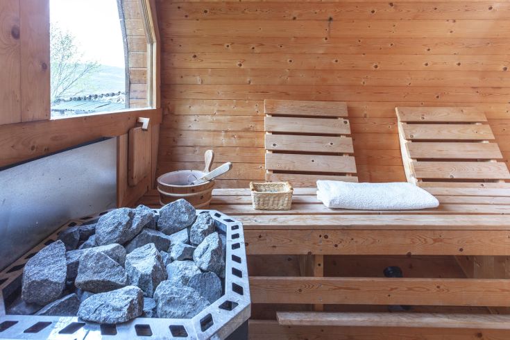 Inside a wooden sauna, furnished with benches and heated stones, perfect for relaxation.