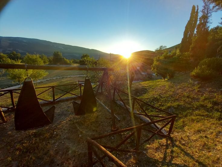 A peaceful sunset at a farmhouse, hills in the background, and swings in the foreground.
