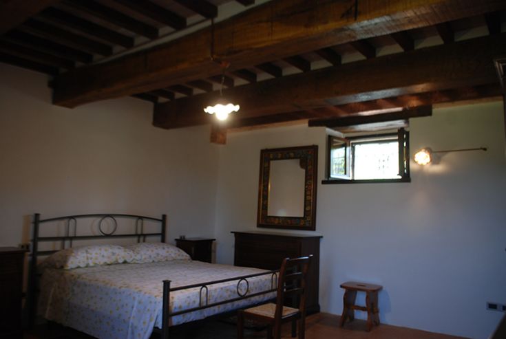 Chambre confortable avec un lit double, décorée dans un style rustique, avec des poutres en bois apparentes au plafond.