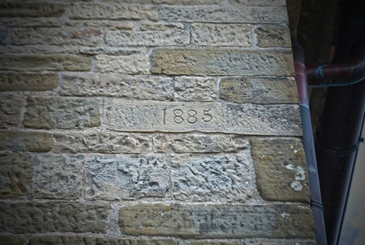 Un mur en pierre avec l'année 1885 gravée, représentant des structures historiques anciennes.