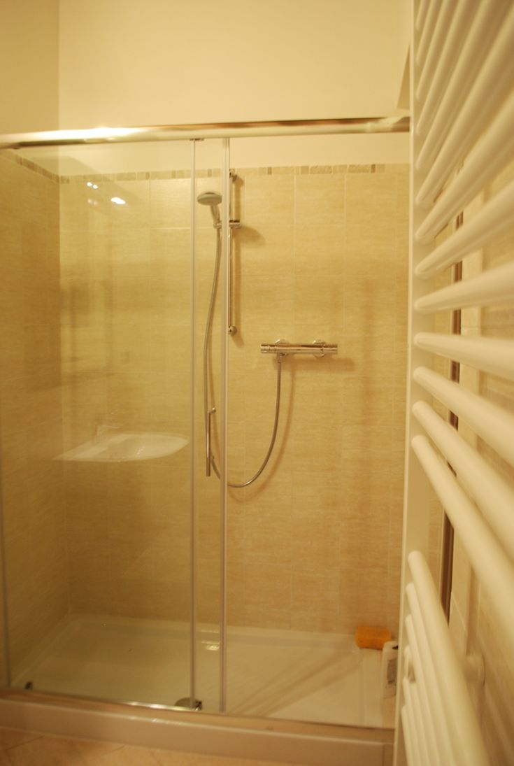 Douche simple avec des portes en verre, des carreaux clairs et des accessoires pratiques.