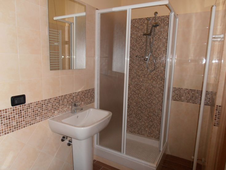 Bagno contemporaneo con doccia, lavabo e specchio, rivestito con piastrelle in toni chiari.