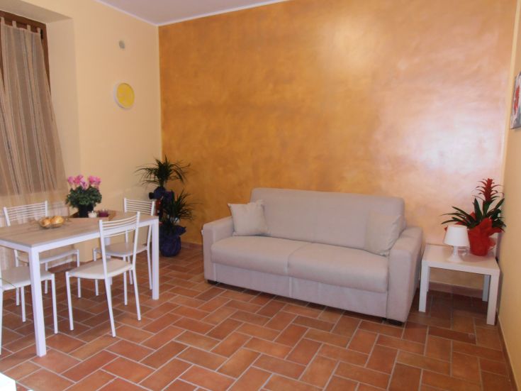 Stanza giorno con divano grigio e tavolo da pranzo, arricchita da alcune piante decorative.