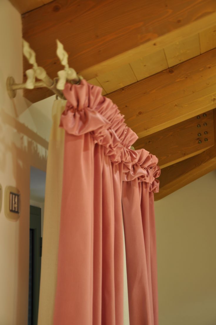 Pink curtains firmly attached to a wooden rod, beneath a wooden ceiling.