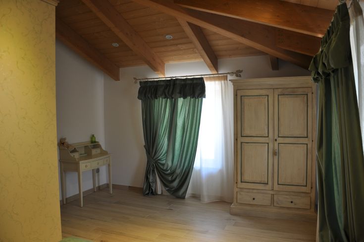 A serene room with exposed wooden beams and green curtains filtering sunlight.
