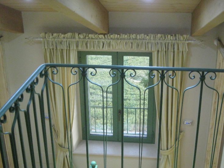 A balcony overlooking a green landscape, featuring a window with simple curtains.