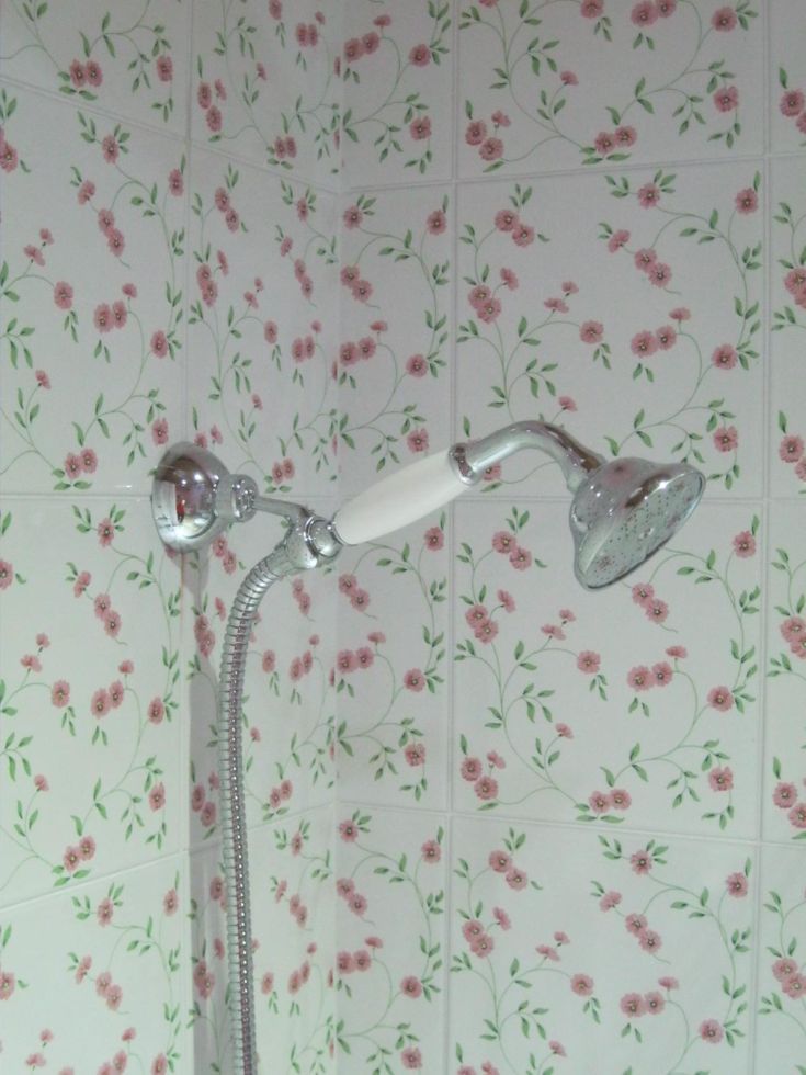 Modern shower with a showerhead over tiled walls decorated with pink floral patterns.