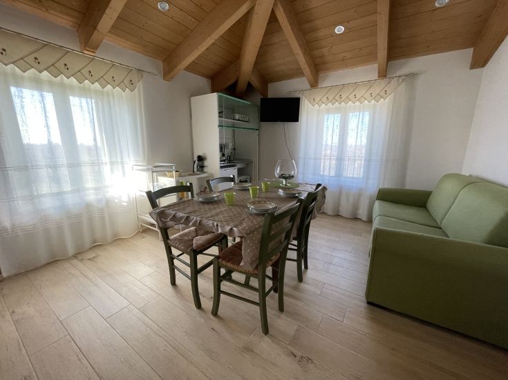 Bright kitchen with equipped cooking area, dining table, and comfy sofa. Light wood dominates the space.