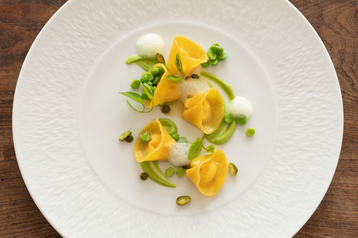 Saffron ravioli with peas and foam decoration, served on a simple plate.