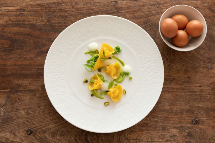 A dish with yellow tortellini and peas, garnished with espuma, presented simply.