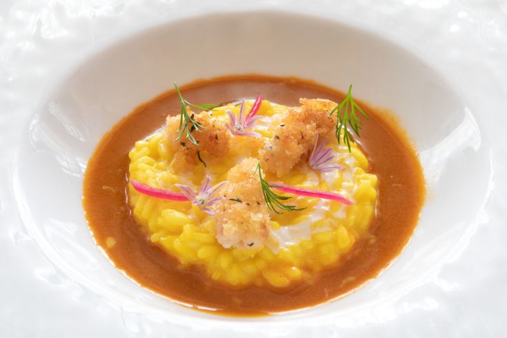 A yellow risotto served with crispy fried items, garnished with flowers and fresh herbs.