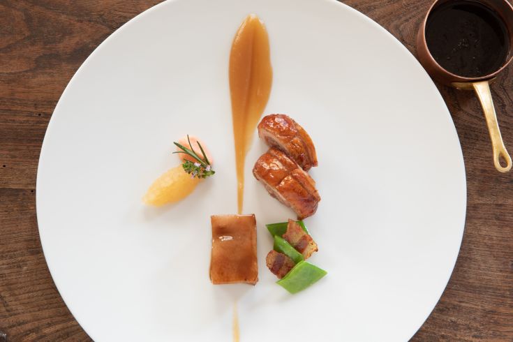 Presentation of a gourmet dish featuring meat, sauces, and colorful side dishes.