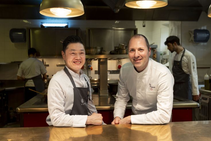 Two smiling chefs in a spacious, well-equipped kitchen, ready to prepare delicious dishes for their guests.