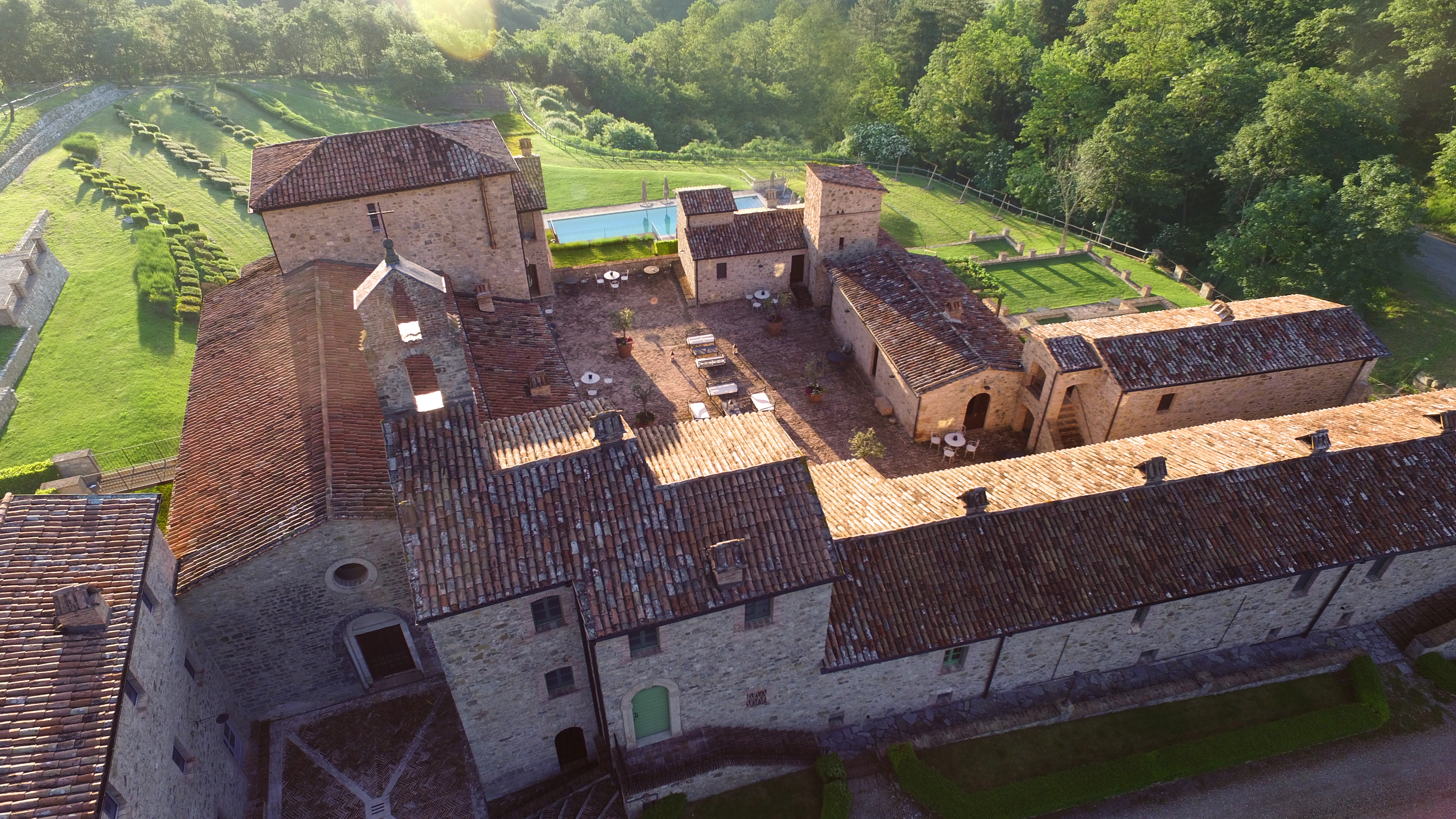 Panorama di un borgo medievale con edifici in pietra e una piscina immersa nel verde circostante.