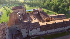A panoramic view of a medieval village with stone buildings and a pool surrounded by lush greenery.