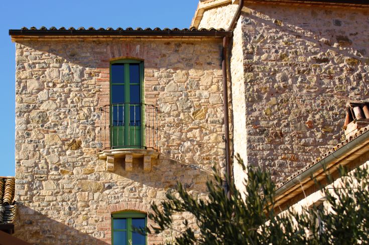 Detail of a stone palace with green windows, typical of an Umbrian village.