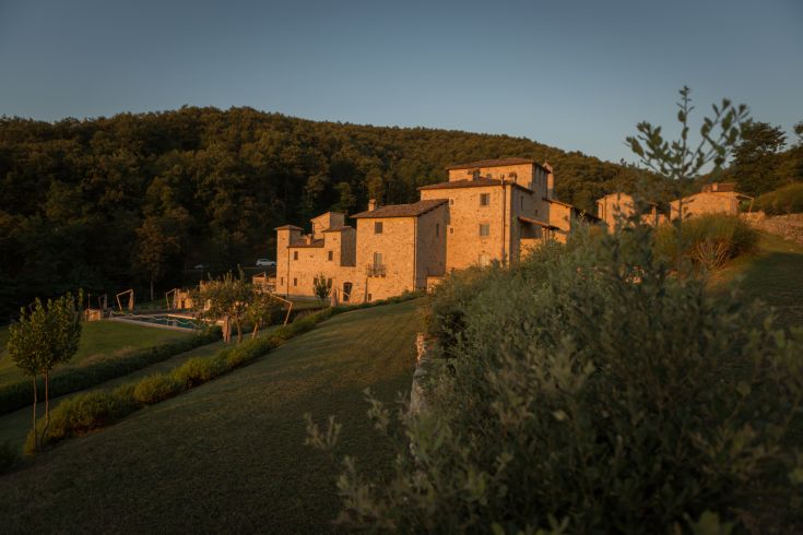 A medieval village surrounded by nature, featuring a historic building, a church, and a relaxation area with a pool.