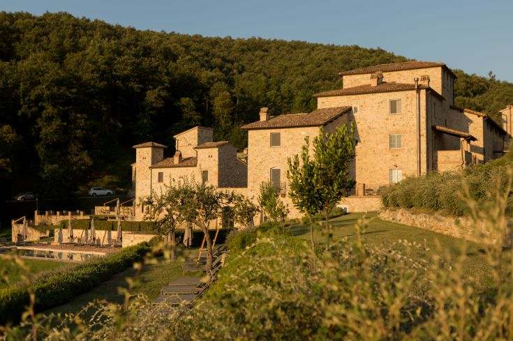 A renovated medieval building surrounded by greenery, featuring an outdoor pool in the garden.