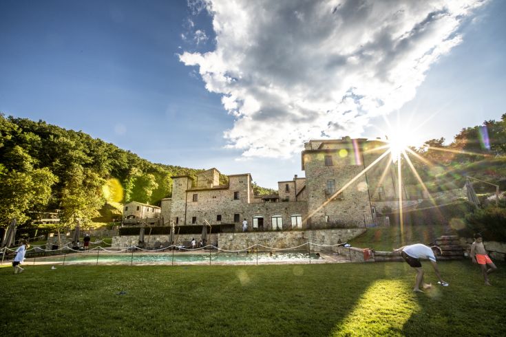 A medieval village surrounded by green hills, with a nature-embedded pool and various relaxation areas.