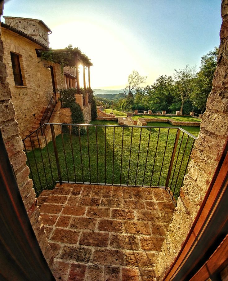 A sunny garden scene featuring trees and flowers, surrounded by a stone building.