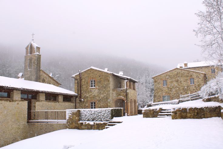 A medieval village in winter, with stone houses and a bell tower, surrounded by a snowy landscape.