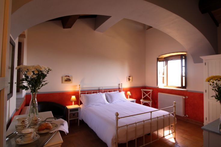 Simple bedroom with a double bed, illuminated by natural light and adorned with flowers.