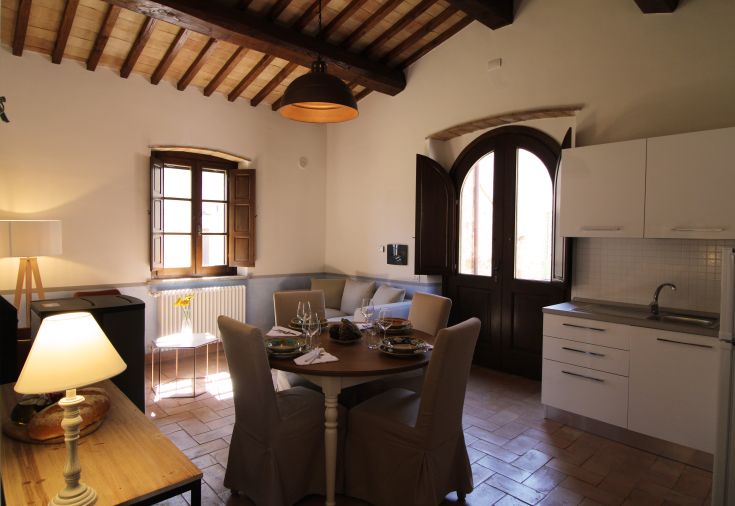 Simple living room with kitchen, featuring arches and wooden beams. Space for relaxation and social moments.