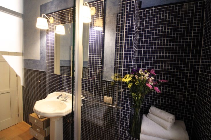 A modern bathroom with blue tiles, soft lighting, and a vase with fresh flowers for a cozy atmosphere.