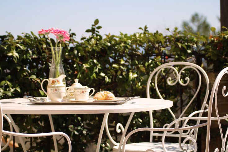 A simple outdoor table set with tea, pastries, and flowers in a peaceful setting.