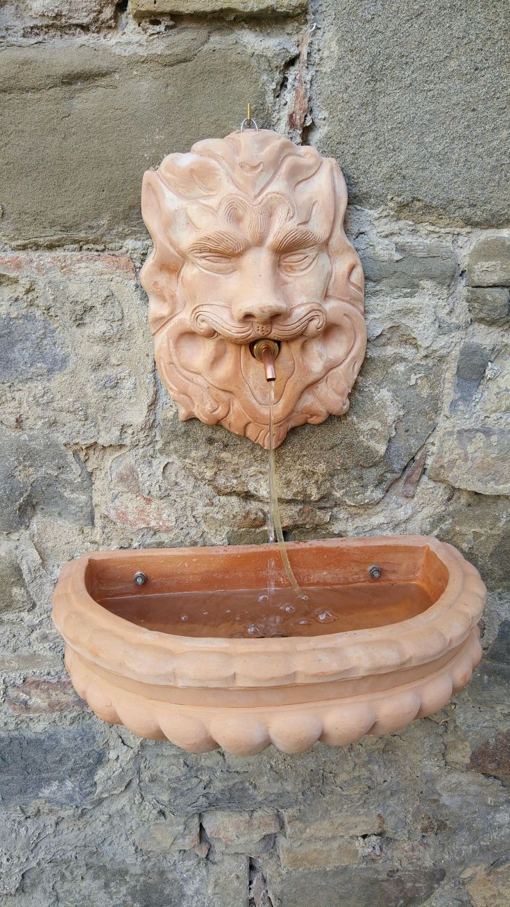 Terracotta fountain with a lion's head, set against a stone wall. A characteristic element of the environment.