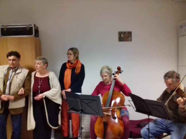 A group of people plays musical instruments in an intimate and relaxed setting.