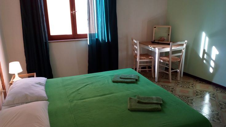 Simple room with a green bed and desk, filled with natural light from the windows.