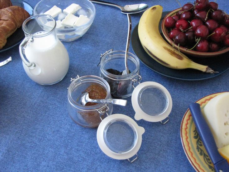 A breakfast table set with milk, fresh fruit, and various jams.