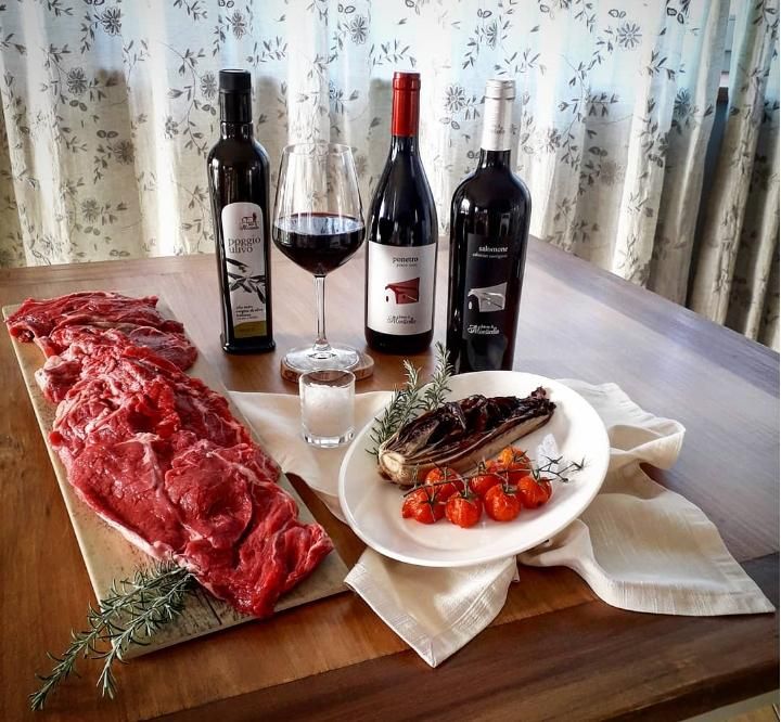 A rustic dining table set with meat, red wine, and tomatoes, surrounded by the tranquility of a farm.