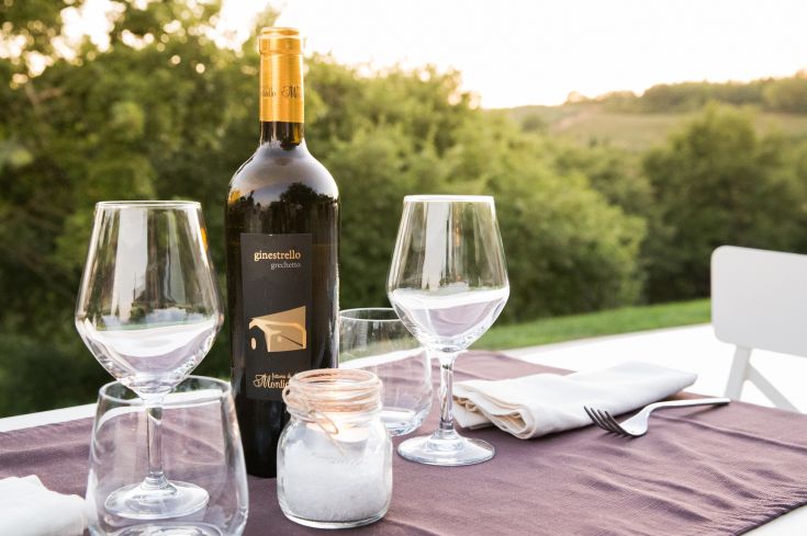 A well-set table with a bottle of wine and glasses, surrounded by a natural setting.