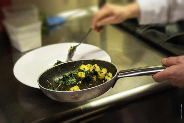 A chef prepares spinach gnocchi in a well-organized and professional kitchen.