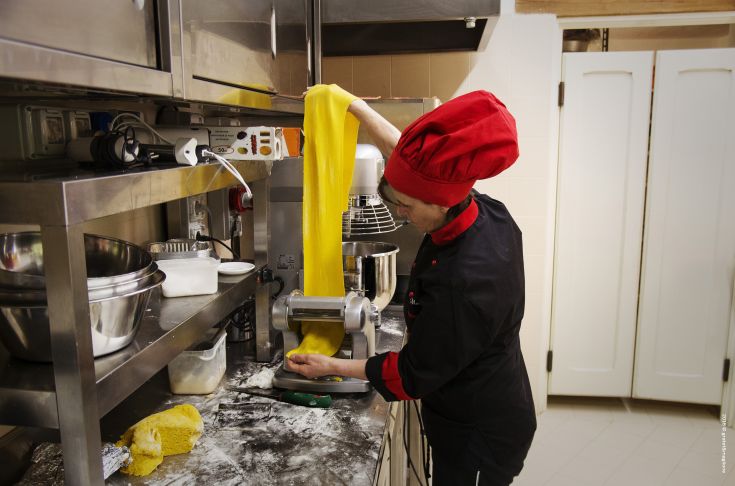 A cook rolling out fresh yellow pasta in a kitchen environment.