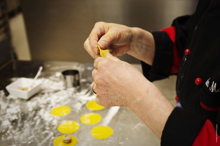 A craftsperson rolls out dough to make fresh ravioli, showcasing their manual skills in culinary preparation.