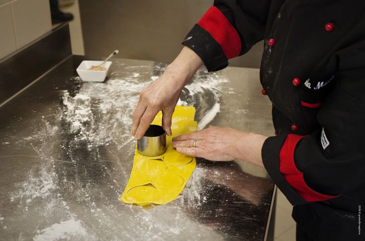 A chef rolling out fresh pasta on a work surface, using a pasta cutter to shape the portions.
