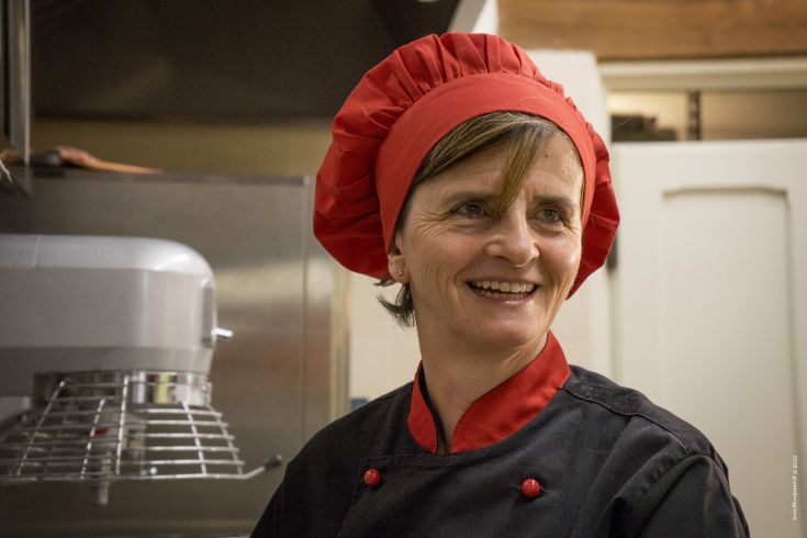 A smiling chef in a professional kitchen, surrounded by utensils and cooking equipment.