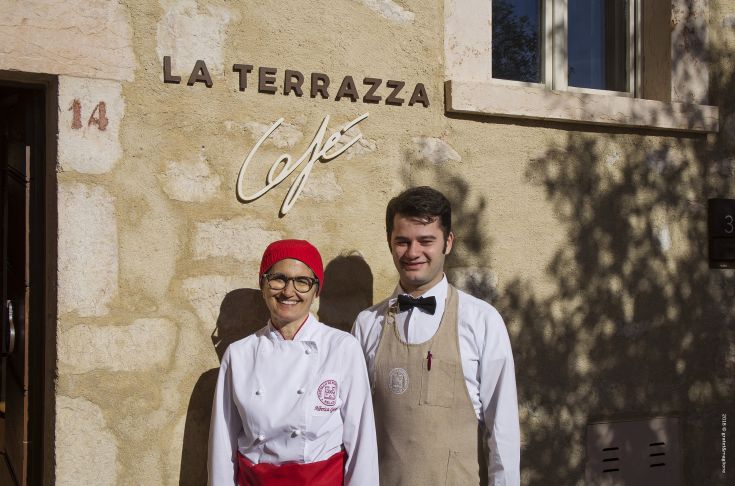 Two smiling chefs at the entrance of a cozy restaurant in an ancient Umbrian village.