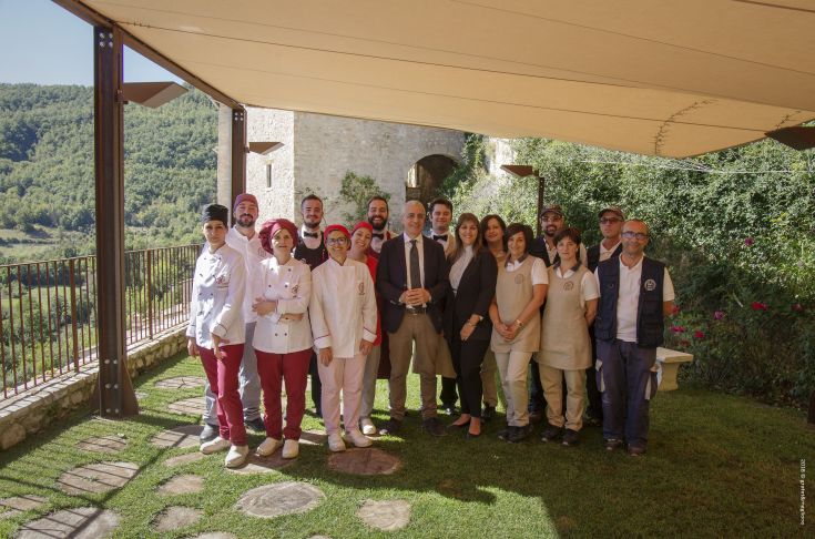 A group of smiling people is gathered outdoors, surrounded by greenery.
