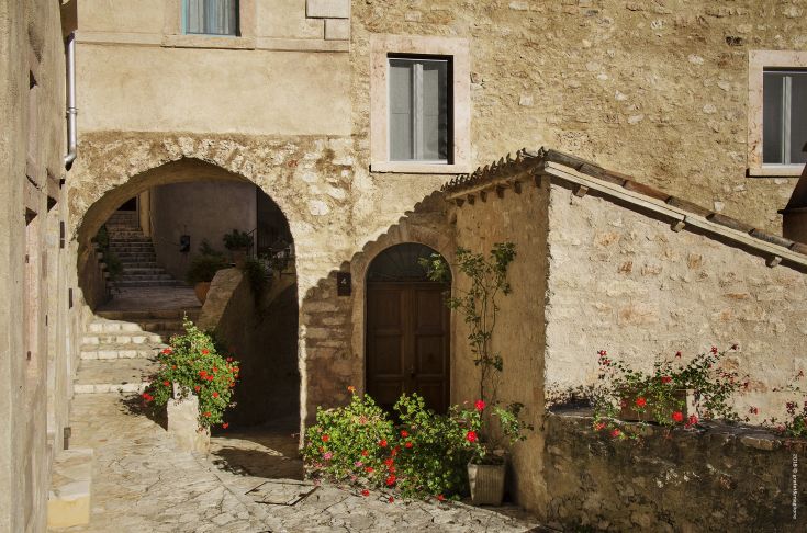 A corner of the medieval village of Postignano in Umbria, featuring flowering plants at the entrance of a building.